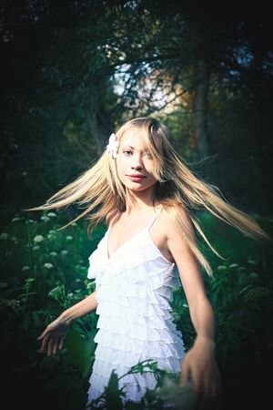 Fairy dancing in the forest. Pretty woman wearied white summer dress is dancing with her hair flying in the air in woodland. Vintage looking image.の写真素材