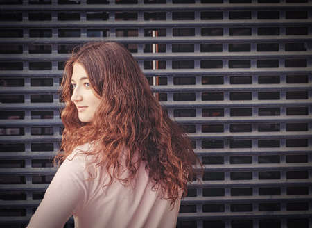 Cute girl with long curly hair looking back in front of metal grid with copyspace. Vintage matte in cross processed fashion.の写真素材