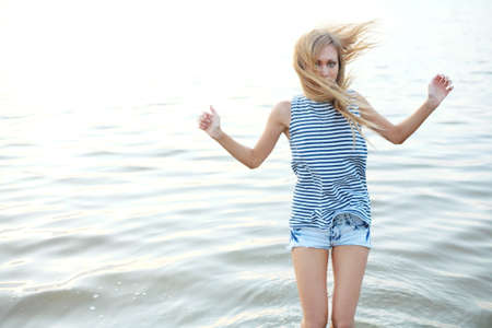 Blond haired woman is standing in the water, her hair is windswept, copyspace on the leftの写真素材
