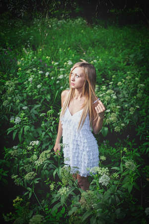Nice lady is wearied white summer press and posing in the woods looking upwards with calm expression on her faceの写真素材