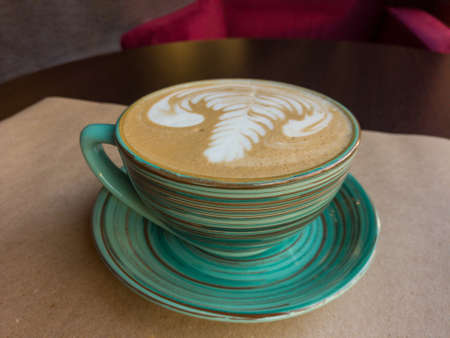 A cup of cappuccino stands on the table. The cup stands on a saucer and both are made in the characteristic sloppy Japanese ceramic style.の写真素材