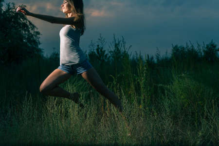 The sporty girl runs in the high grass at night. She dances or jumps full of young fever and energy.の写真素材