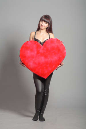 Slender girl is holding giant heart in front of her, fullbody shot.の写真素材