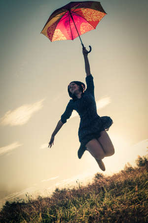 The girl jumped up holding a colored umbrella against the sky in the retro-colored film photoの写真素材