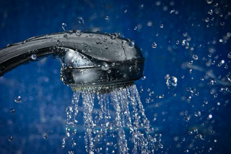 Shower head in front of blue wall of bathroom full of steam with water drops flying around, shot with copyspace.の写真素材