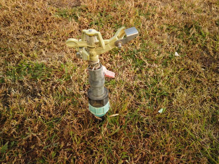Weathered sprinkler is resting in the field of dry grass after summer seasonの写真素材