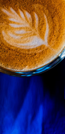 Latte art on the top froth of the flat white coffee servrd in small glass on blue background, top viewの写真素材