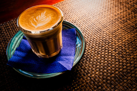 Flat white coffee is served on saucer over the table with bamboo mat backlit, copyspaceの写真素材
