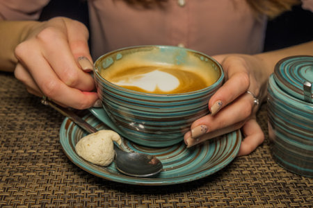 A ladys hands with latte coffee on a wood table with bamboo mat.の写真素材