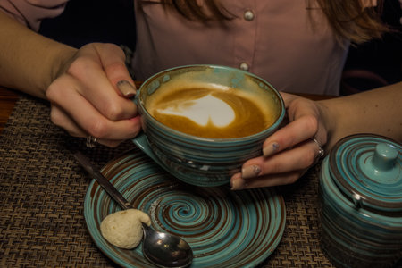 Mug of coffee on a wooden table with sugarbowl , the girl holds in her hand one cup of milk coffee in an air. A photo depicting a cosy relaxing coffeebreakの写真素材