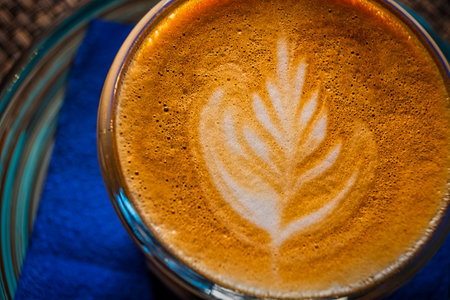 Froth art on the top froth of the flat white coffee servrd in small glass on blue background, top view macro image.の写真素材
