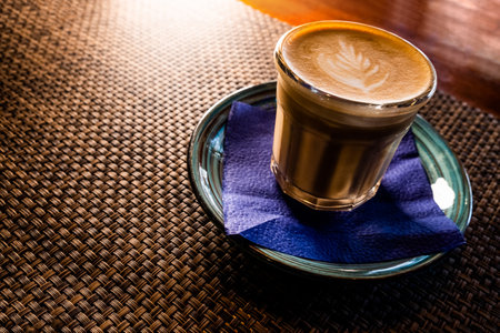 Flat white coffee froth art on top is served on saucer over the table with bamboo mat backlit, copyspaceの写真素材