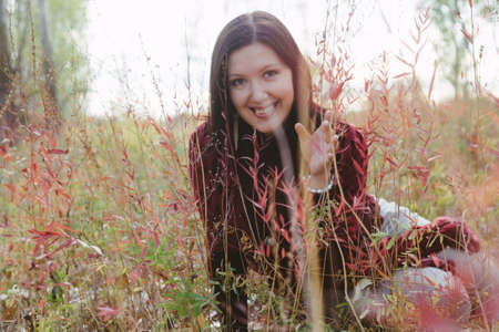 Happy dark-haired lady smiling in bitween red autumnal grass steams.の写真素材