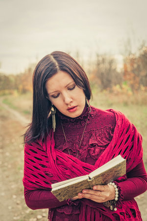 Dark-haired lady In park with old poetry book reading vintage dressedの写真素材