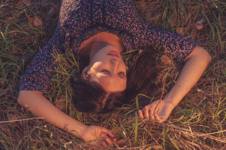 Calm girl in vintage clothes lying on brown grass. Fashionable lady wearing a ornate print is having relax with on the lawn. Leisure in rural area.の写真素材
