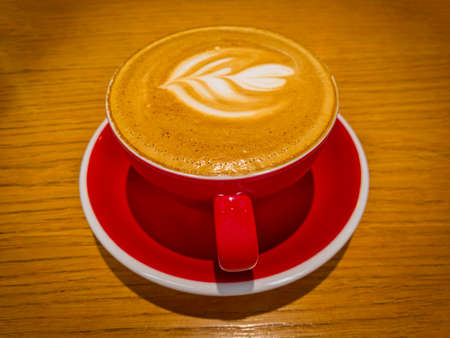 Latte Art On Froth. Hot latte coffee on wooden table. Morning with a red cup of cappuccino. Art and craft coffee.の写真素材
