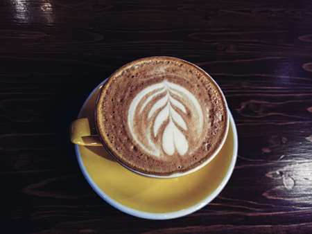 Cappucino cup with ornate froth art heart shape on yellow saucerの写真素材