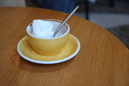 Empty coffee cup of yellow color is standing on light wooden tableの写真素材