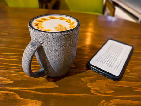 Mobile office. Cup of coffee with froth art on top served on desk with some mobile gadget lying near on desk, above view.の写真素材