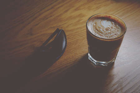 Coffeee cup on wooden table with sunglasses lying near, vintage low-light shot imageの写真素材