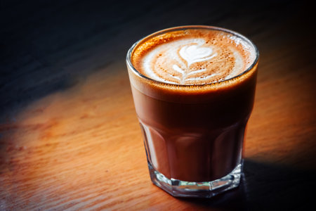 Flat-white coffee cup served on wooden table in spot of light, copyspace on leftの写真素材