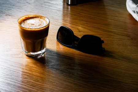 Flat white coffee served on table and sunglasses lay near, copyspace on foreground.の写真素材