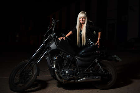Sexy biker girl is posing on motorcycle in the night. She is happy looking at camera.の写真素材