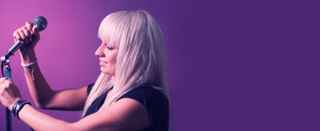 Blond haired woman set up the mic on mic-stand on pink violet background with a lot of copyspace. Banner for web site.の写真素材