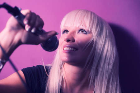 Blond model girl singer with a mic on pink background.の写真素材