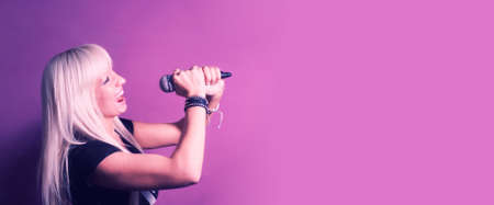 Portrait of a charismatic blonde woman singing with microphone in studio over pink background, banner mock-up.の写真素材