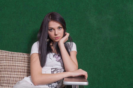Lady with blank expression. 20s brunette indoors sitting against green wallの写真素材