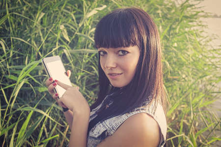 Brunette holds a tablet touch pad computer gadget with green screen outside in the summer and point at screen while on adventure.の写真素材
