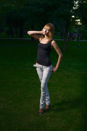 Blond girl with short hair standing cross legged alone in the falling dark at cemetery lawn.の写真素材