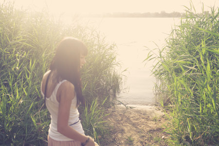 Backlit silhouette of girl alking towards the pond with reeds candid shot with flares low contrast, joy and fun in summer, summertime mood.の写真素材