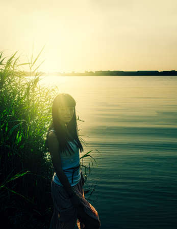 Melancholy solitude in deserted place. Lonely girl standing in reeds aside the pondの写真素材