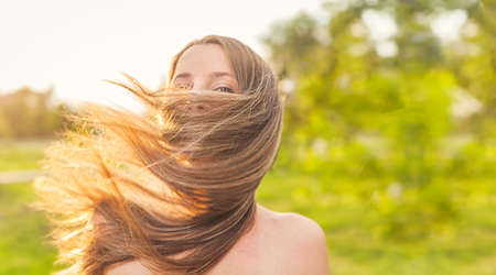 Happy lady face wrapped in her long blond hair by blow of the wind, joyness and freedome outside, warm summertime image.の写真素材