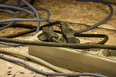 Messy outlet power extension cord on an apartment floor with plugs plugged in. Cable power cords in a tangled mess on floor of workplace, used dirty electric outlet.の写真素材