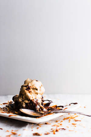A plate with a spoon and a decadent chocolate cake topped with melting ice cream and fudge sauce.の写真素材