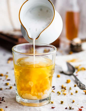 Foamy milk pouring into a glass filled with yellow chamomile teaの写真素材