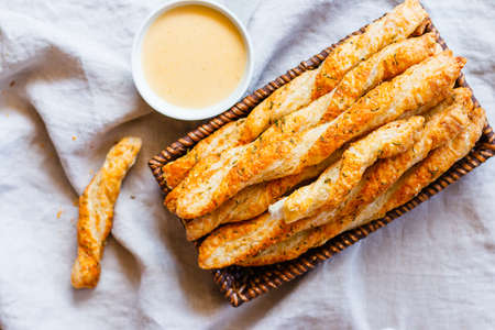 Cheesy puff pastry twists in a basket near a bowl of cheese sauceの写真素材