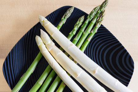 White and green asparagus on a black plate on a wooden tableの写真素材