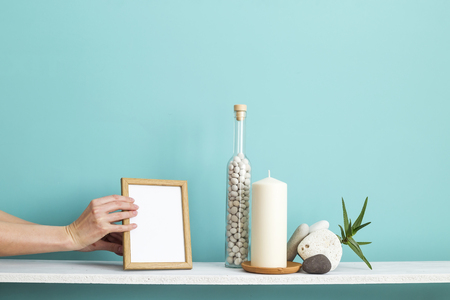 Modern room decoration with Picture frame mockup. White shelf against pastel turquoise wall with Candle and rocks in bottle. Potted succulent plantの写真素材