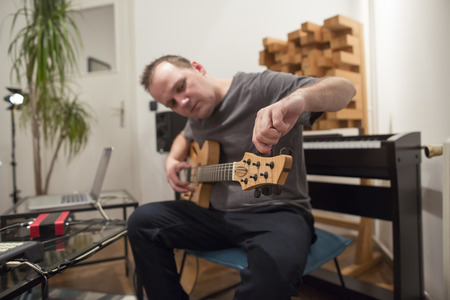 Professional musician tuning electric guitar in digital studio at home. He is surrounded with instruments and midi controller. Music production concept.の写真素材