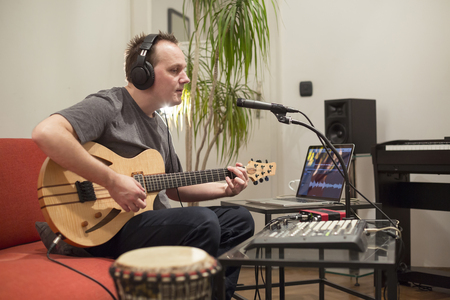 Professional musician recording electric guitar in digital studio at home. He is surrounded with instruments and midi controller. Music production concept.の写真素材