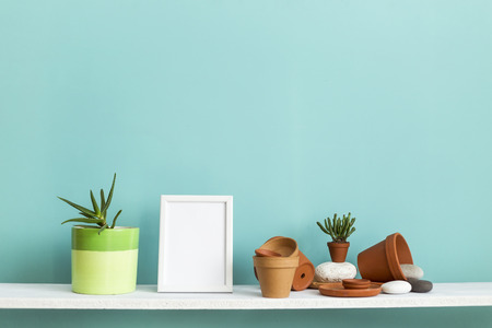 Modern room decoration with picture frame mockup. White shelf against pastel turquoise wall with pottery and succulent plant with potted succulent plant.の写真素材