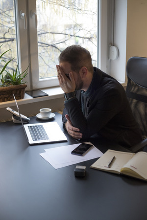 businessman working on laptop in office making phone call nervous and angry by window black table with notebook papers phoneの写真素材
