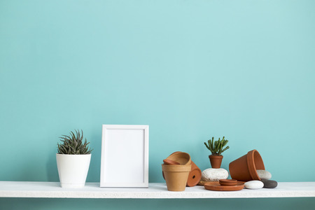 Modern room decoration with picture frame mockup. White shelf against pastel turquoise wall with pottery and succulent plant with potted succulent plant.の写真素材