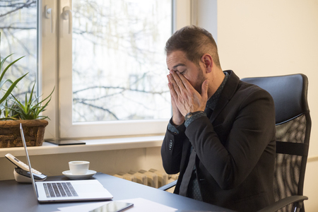 businessman working on laptop in office eyes hurt by window black table with notebook papers phoneの写真素材