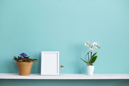 Modern room decoration with Picture frame mockup. White shelf against pastel turquoise wall with potted orchid and violet plant.の写真素材