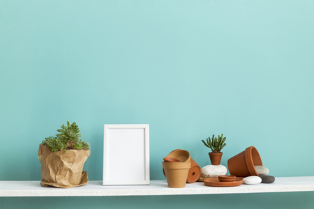 Modern room decoration with picture frame mockup. White shelf against pastel turquoise wall with pottery and succulent plant with potted succulent plant.の写真素材